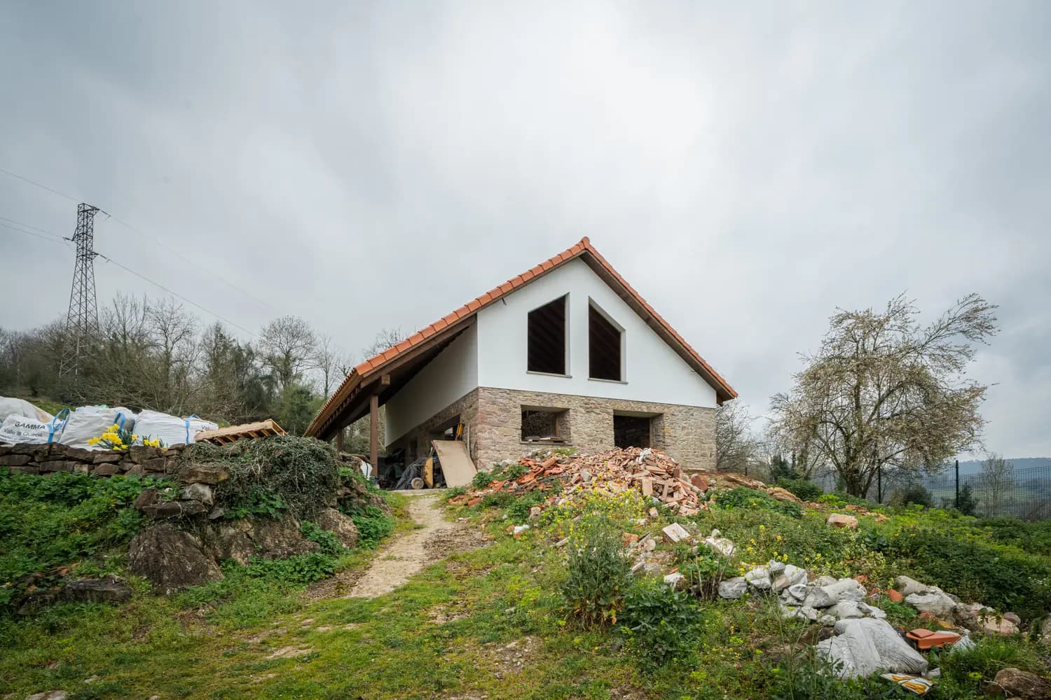 Casa de piedra en rehabilitación en una ladera de Asturias, con material de obra en la parcela