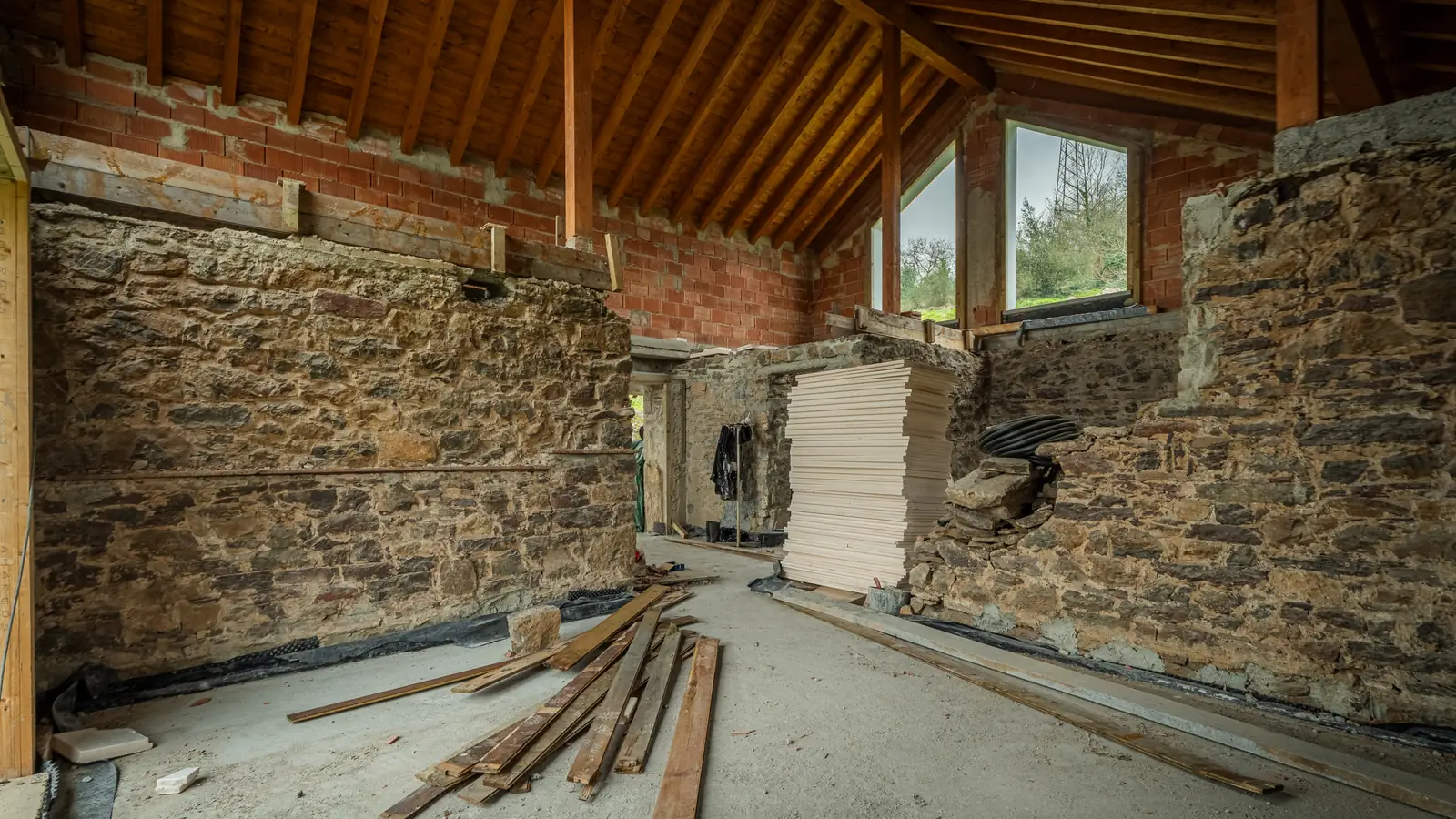Interior de una vivienda de piedra en rehabilitación, con estructura de madera nueva y material apilado